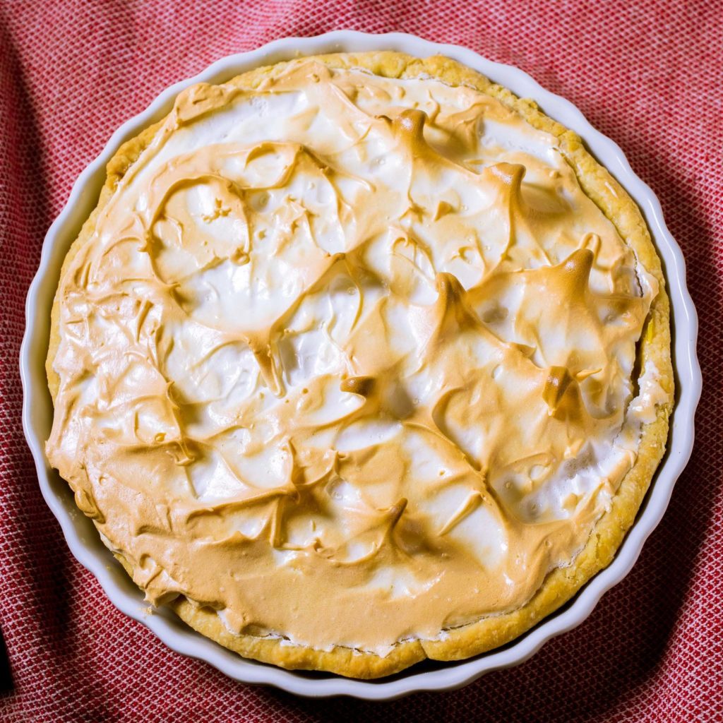A whole, uncut lemon meringue pie from the top, sitting on a red gingham cloth.