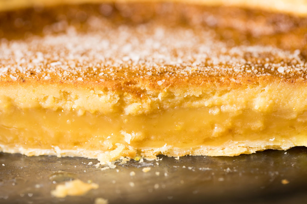 Side view of a cut pie. The custard baked into layers—the top is thin, golden brown sprinkled with salt. Next down is a dense, light yellow. The thickest layer is gooey and golden, sitting ontop a thin layer of crust.