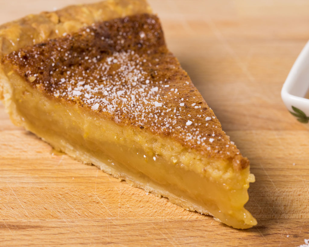 A wedge of Salted Honey pie sitting on a cutting board.
