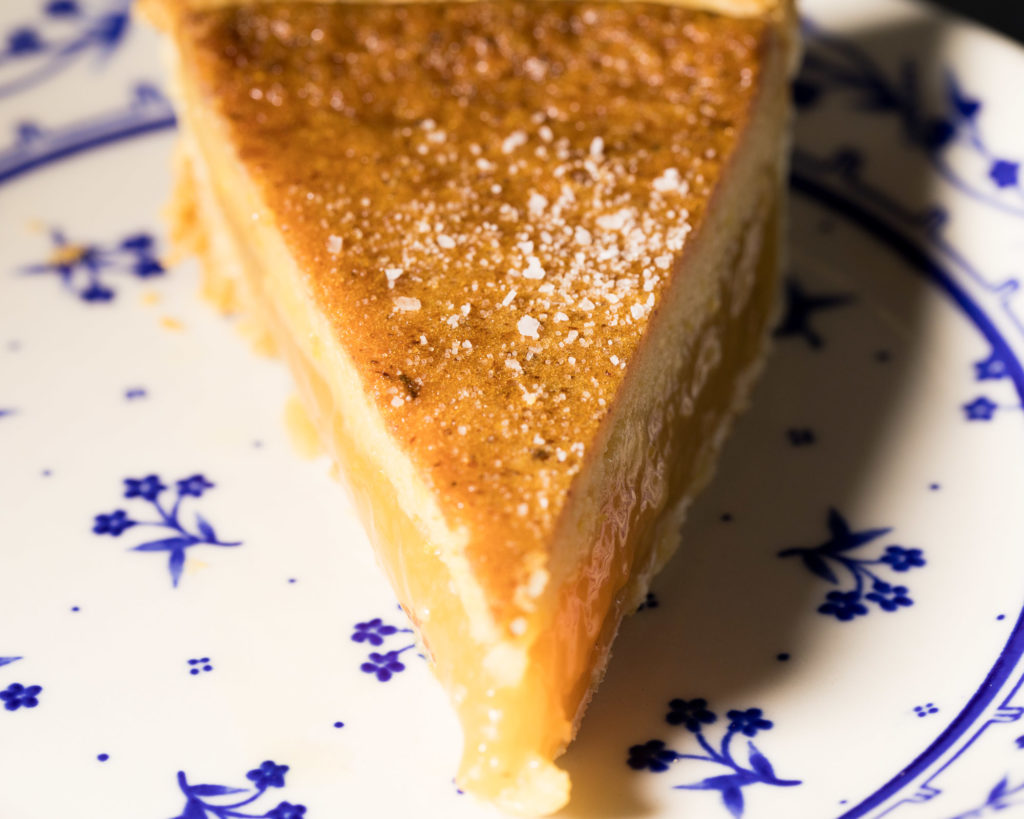 A wedge of Salted Honey Pie sitting on a white plate with a small blue flower pattern.